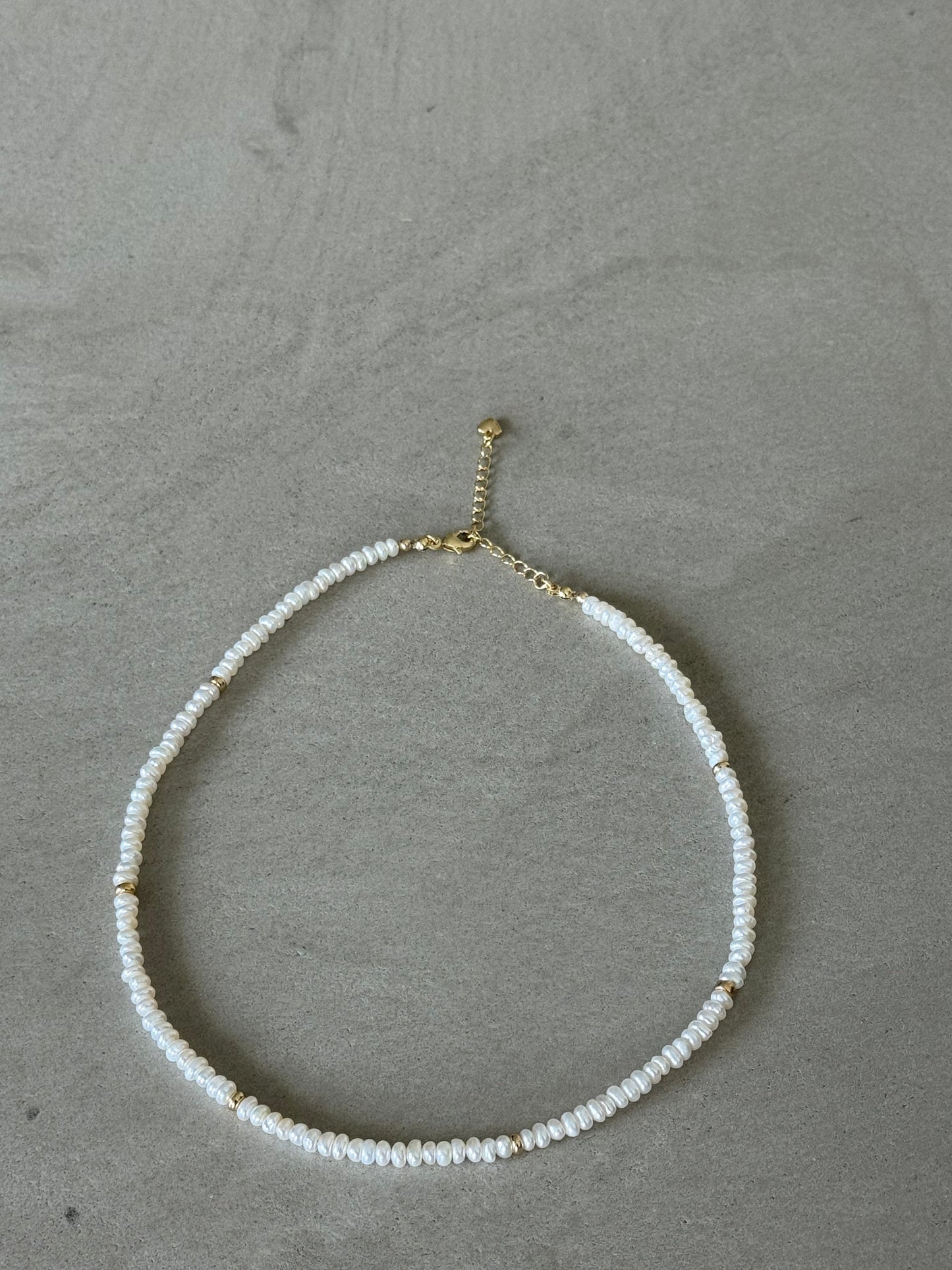 Necklace with white beads and gold clasp on a gray surface