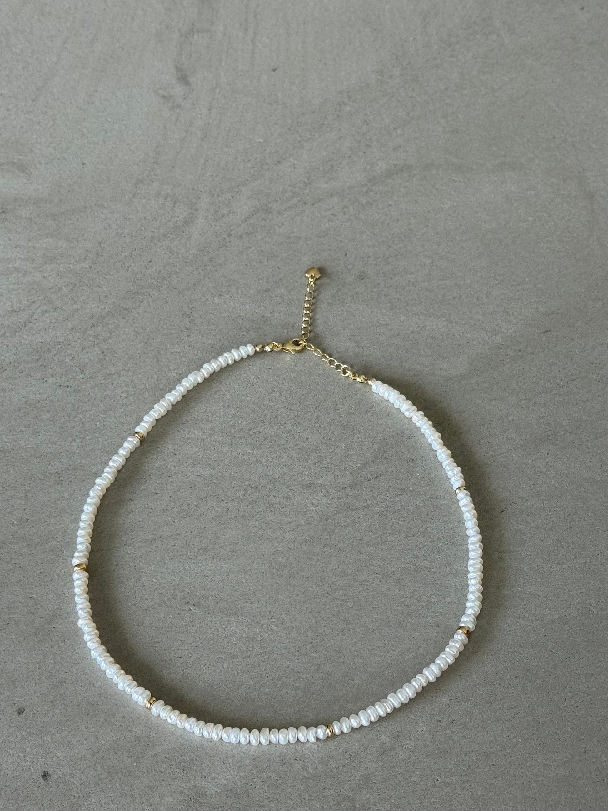 Necklace with white beads and gold clasp on a gray surface