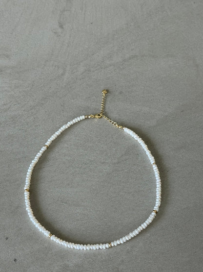 Necklace with white beads and gold clasp on a gray surface